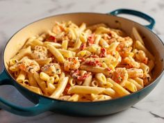 a blue pot filled with pasta and sauce on top of a counter next to a wooden spoon