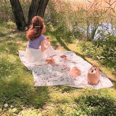 a woman sitting on top of a blanket next to a tree and holding a basket