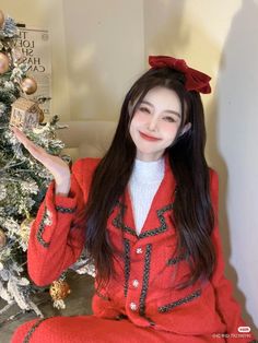 a woman sitting in front of a christmas tree with her hand up to the camera