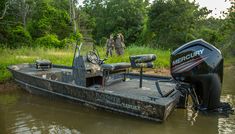 two men standing on the back of a boat in water next to grass and trees