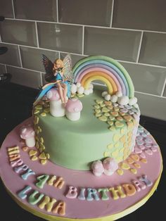 a birthday cake with a fairy sitting on it's top and rainbow decorations around the edges