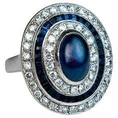 Belgium, 1940s The ring is handcrafted in 18K white gold. It is centered with a cabochon cut blue sapphire encircled by two rows of diamonds (about 1 carat total weight) and a row of channel-set French cut sapphires. The cabochon sapphire measures 8.6 x 6 x 4.4 mm and is approximately 2.45 carats. Combined diamond weight is about 1 carat. Marked with maker’s initials ‘GA’ and Belgian assay mark for 750 gold (18K). The bezel measures 20 x 17 mm (13/16 x 11/16 in.). Ring size 4.75 (15 mm) resizabl Rings With Sapphires, Diamond White Gold Engagement Ring, Enagement Rings, Blue Sapphire Engagement Rings, Wedding Bands For Men, Diamond Engagement Rings Cushion, Jewelry Sapphire, Ruby And Sapphire, Necklaces Statement