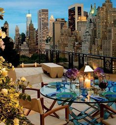 an outdoor dining table with candles and flowers on it in front of the city skyline