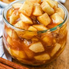 a glass jar filled with apple slices on top of a table next to cinnamon sticks