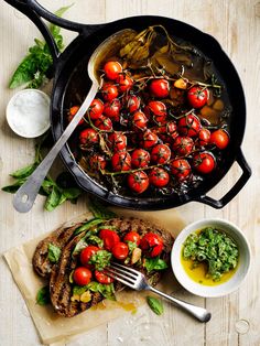 a pan filled with lots of food on top of a wooden table next to a knife and fork