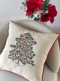 a christmas tree pillow sitting on top of a couch next to a vase with red flowers