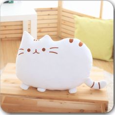 a white cat pillow sitting on top of a wooden table