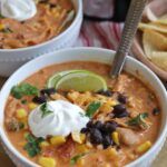 two bowls of mexican soup with sour cream and tortilla chips on the side