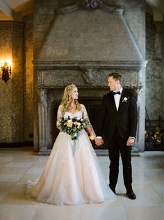 a bride and groom holding hands in front of a fireplace