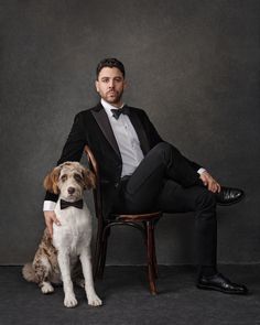 a man in a tuxedo sitting on a chair next to a brown and white dog