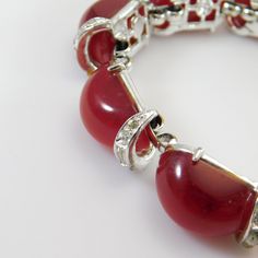 Kramer red moonglow bracelet is a beautiful example of mid-century costume jewelry. Unique dome shaped deep red moonstones are set in silver tone metal. Curved spacers are on the end of each link and are set with baguette rhinestones and tiny chatons. The lovely Kramer bracelet is about 1/2 inch wide and about 6 3/4 inch long, closing with a fold over clasp. Top to bottom the bracelet sits about 3/8 inches off the base. There are two tiny chatons missing and some slight yellowing a few stones bu Retro Red Bracelet Jewelry, Vintage Red Gemstone Bracelets, Vintage Rhinestone Jewelry, Daisy Jewelry, Costume Jewelry Rings, Purple Daisy, Mid Century Jewelry, Rhinestone Ring, Moon Glow