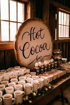 a table filled with lots of cups next to a sign that says hot cocoa bar