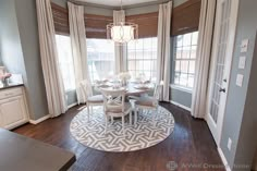 a dinning room table and chairs in front of two windows