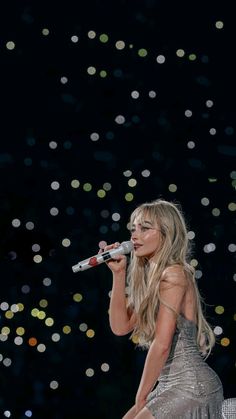 a woman in a silver dress is holding a microphone and singing into the air with confetti all around her