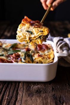 a person is holding up a piece of bacon and spinach casserole in a white dish