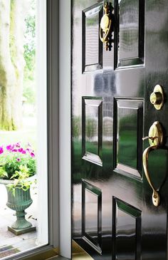 a black door with brass handles in front of a window and potted plants outside