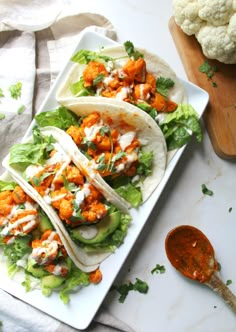 three tacos on a plate with sauce and cauliflower