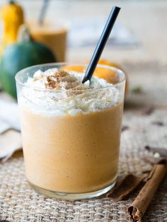 a drink with whipped cream and cinnamon on the side, next to an orange pumpkin