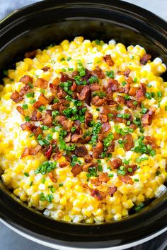 a crock pot filled with corn, bacon and green onions on top of it