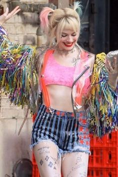 a woman in short shorts and a pink top with fringes on her arms is walking down the street