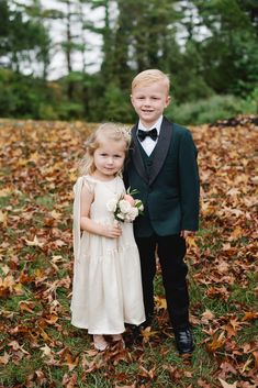 a young boy and girl dressed in formal wear posing for the camera with leaves on the ground