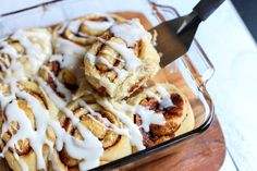 cinnamon rolls with icing in a glass dish on a wooden cutting board next to a knife