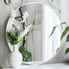 a white vase filled with flowers sitting on top of a table next to a mirror