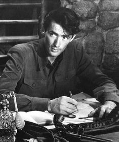 a man sitting at a desk writing on a piece of paper with an old typewriter in front of him