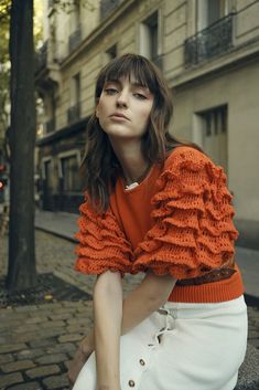 a woman in an orange sweater and white skirt