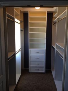 an empty walk in closet with white shelves and drawers on each side, along with carpeted flooring