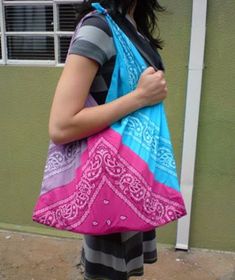 a woman carrying a large pink and blue bag on her back while standing in front of a building