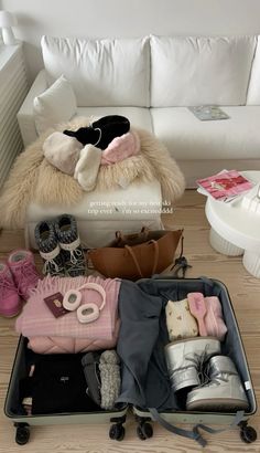 an open suitcase filled with clothes and shoes on a wooden floor next to a white couch