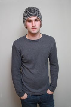 a young man wearing a knitted hat standing in front of a wall with his hands in his pockets