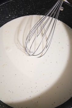 a whisk is being stirred in a pan with white liquid on the side