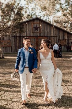 a bride and groom walking hand in hand through the grass at their rustic barn wedding