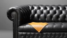 a black leather couch with a yellow throw pillow on it's arm and back