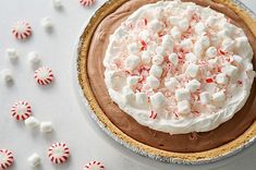 a chocolate pie with marshmallows and candy canes around it on a white table