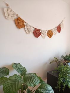 there is a plant in the corner next to a wall hanging with tassels on it