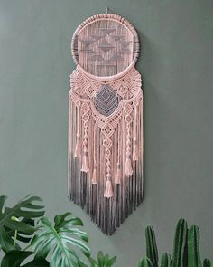 a pink wall hanging with tassels on it next to a potted plant