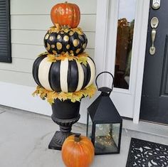 three pumpkins are stacked on top of each other in front of a house with a lantern