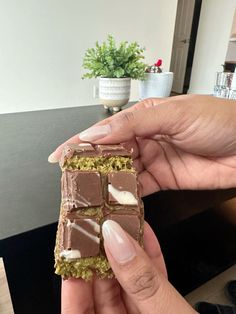 a hand holding a piece of chocolate with white frosting and green sprinkles