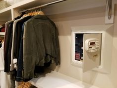 a closet with clothes hanging on the wall and an alarm clock mounted to the wall