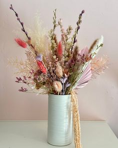 a white vase filled with lots of different types of flowers on top of a table