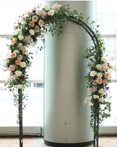 an arch decorated with flowers and greenery stands in front of a window at the end of a room