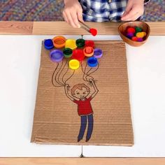 a young boy is painting on a piece of cardboard with colored crayons in front of him