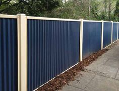 a blue and white fence next to a sidewalk with trees in the backgroud