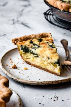 a slice of quiche on a plate with a fork next to it and another pie in the background