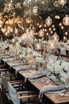 a long table with many lights hanging from the ceiling and flowers in vases on it