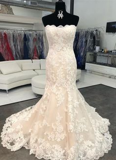 a white wedding dress on display in a room with lots of clothes hanging up behind the mannequin