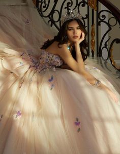 a woman in a ball gown with a tiara sitting on a stair case holding her hand to her face